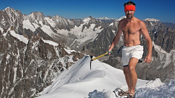 Wim Hof wearing a red headband, white shorts and carrying a pickaxe standing atop Mount Everest in the snow