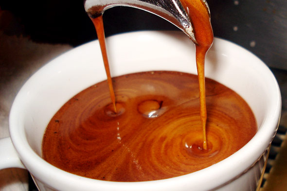 Coffee being poured from an expresso machine into a white ceramic cup