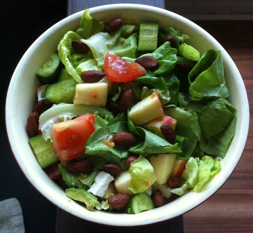 A salad with greens, apple, tomato, nuts and feta cheese