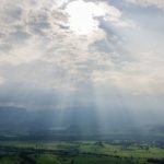 Sun rays shining through the clouds onto a city with green grass around