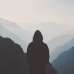 Hooded man standing in front of mountain range