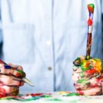 Man wearing shirt holding messy paintbrushes to represent contrast between trait openness and trait conscientiousness